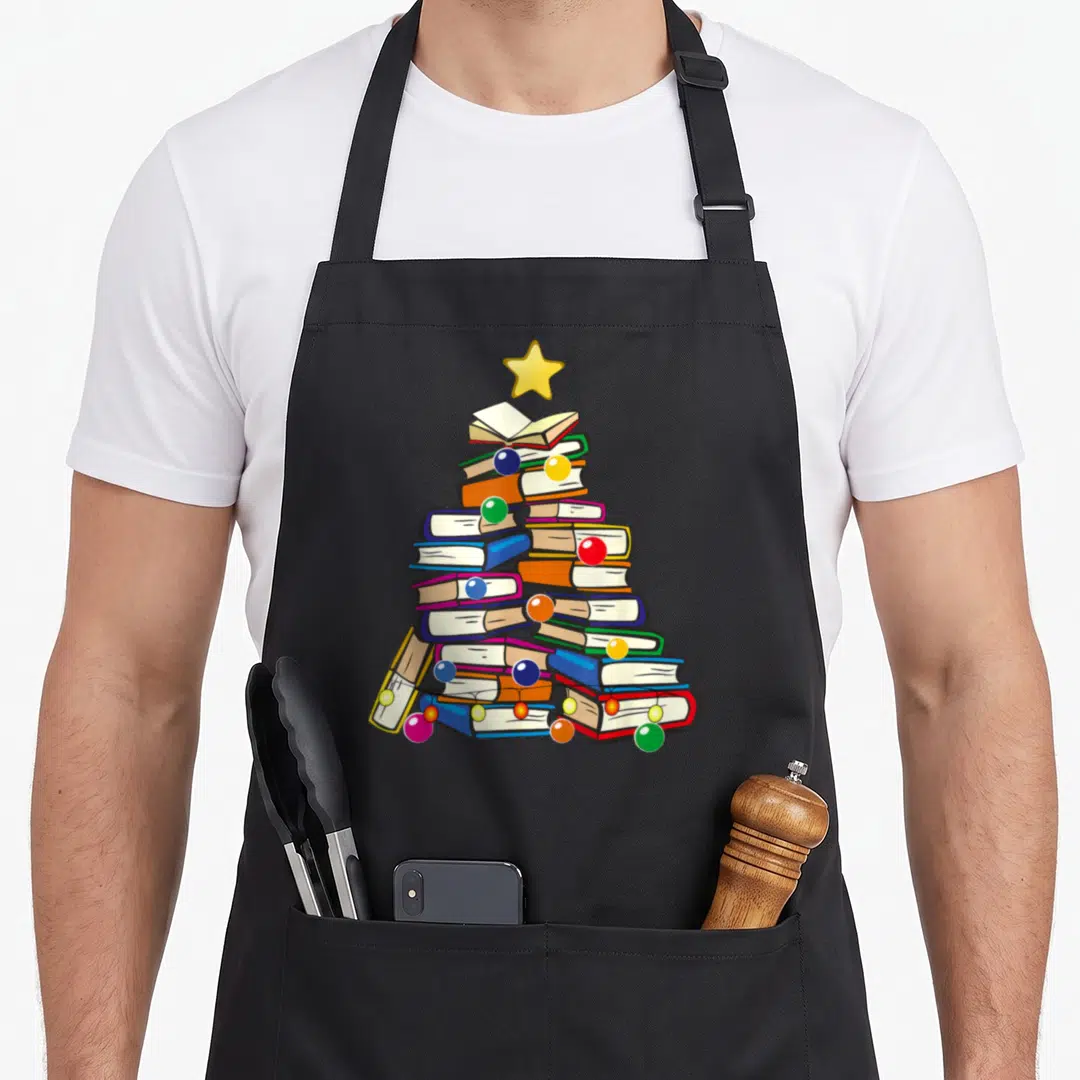 Reading christmas tree apron - Cartoon stack of books shaped like a Christmas tree with colorful ornaments and a star — shown on a black cotton canvas apron against a white background