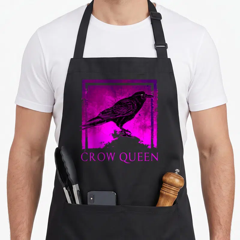 Queen bird aprons - Black crow illustration inside distressed purple and pink square with CROW QUEEN text below — shown on a black cotton canvas apron against a white background