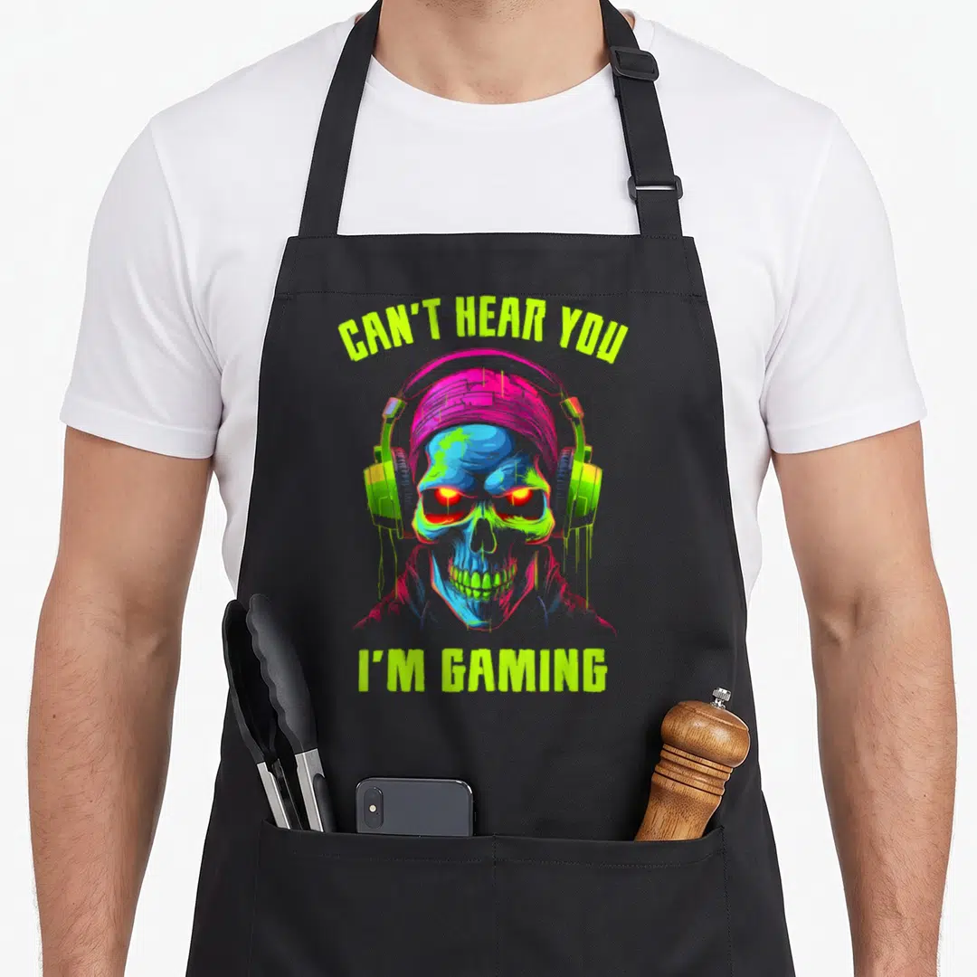 Skull gaming apron - Colorful skull wearing headphones with arched lime green text reading Can't Hear You I'm Gaming — shown on a black cotton canvas apron against a white background
