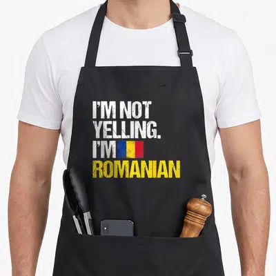 Yelling romanian apron - I'M NOT YELLING I'M ROMANIAN text with small tricolor flag on black background — shown on a black cotton canvas apron against a white background