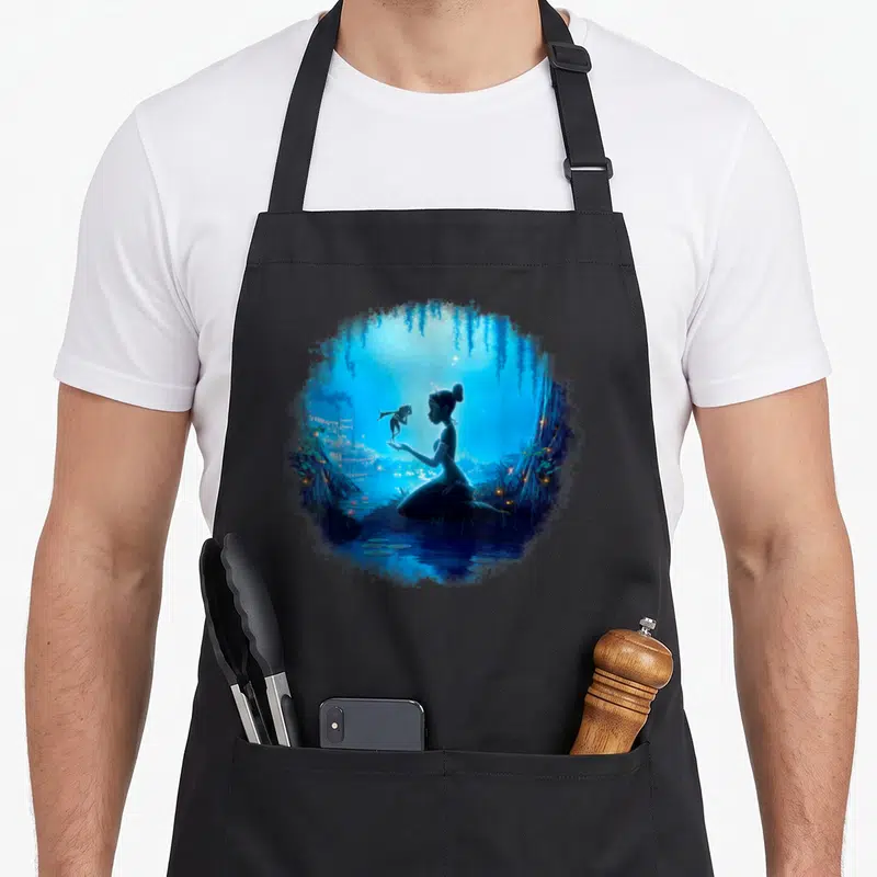 Swamp princess apron - Circular watercolor of woman silhouette holding frog in blue night swamp with willow branches — shown on a black cotton canvas apron against a white background