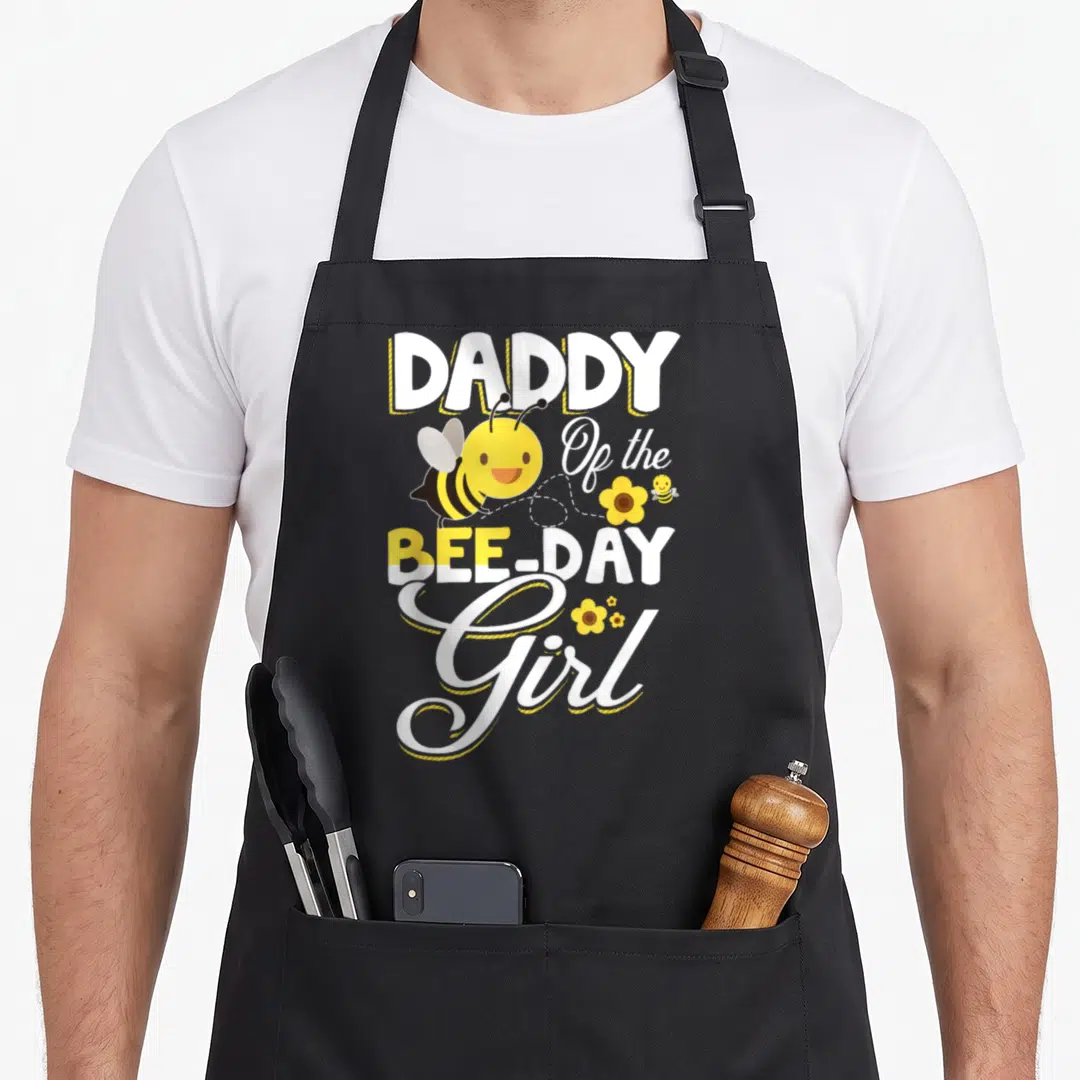 Daddy bee aprons - Cartoon bee and flower graphic with Daddy of the Bee Day Girl text — shown on a black cotton canvas apron against a white background