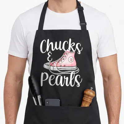 Pearl us aprons - Pink sneaker with draped pearl necklace and text Chucks & Pearls — shown on a black cotton canvas apron against a white background