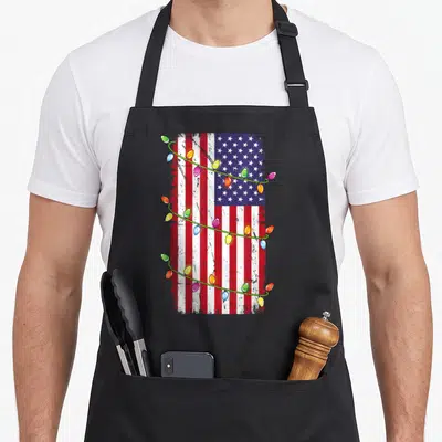 Flag christmas lights apron - Distressed USA flag with red white blue stripes and multi-colored Christmas light strings — shown on a black cotton canvas apron against a white background