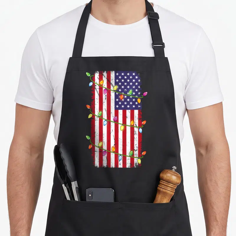 Flag christmas lights apron - Distressed USA flag with red white blue stripes and multi-colored Christmas light strings — shown on a black cotton canvas apron against a white background
