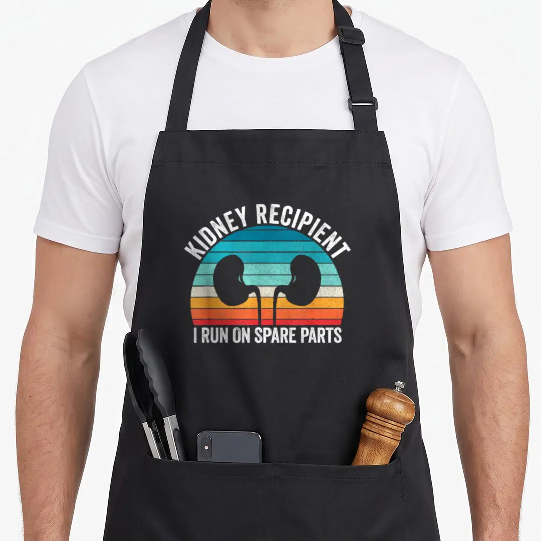 Run parts of an apron - Two kidney silhouettes over striped retro sunset with white text reading Kidney Recipient and I — shown on a black cotton canvas apron against a white background
