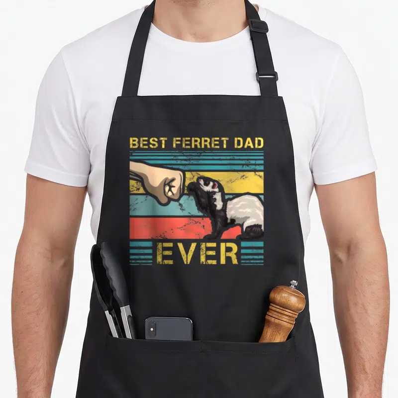Ferret father day apron - BEST FERRET DAD EVER text above and below ferret hand fist bump on yellow blue red black — shown on a black cotton canvas apron against a white background