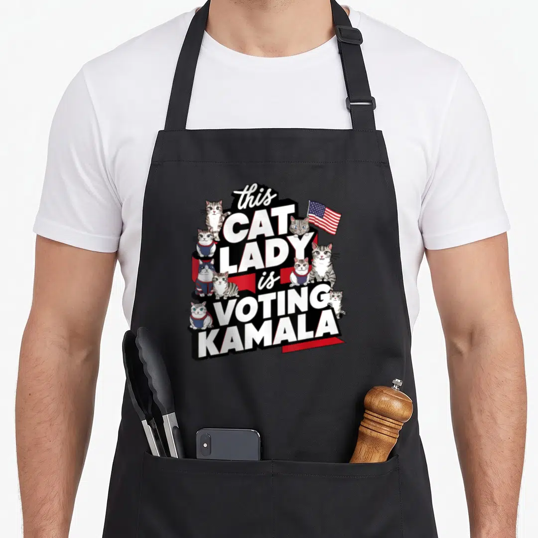 Voting cat lady apron - Stacked text this CAT LADY is VOTING KAMALA surrounded by cartoon cats and USA flag — shown on a black cotton canvas apron against a white background