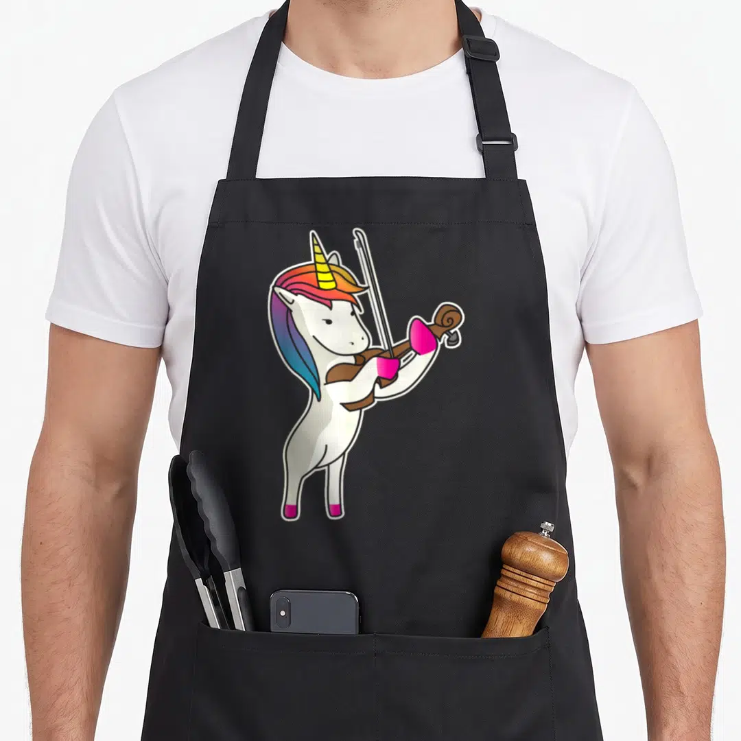 Playing unicorn apron - White cartoon unicorn standing playing brown violin with rainbow mane and pink hooves — shown on a black cotton canvas apron against a white background