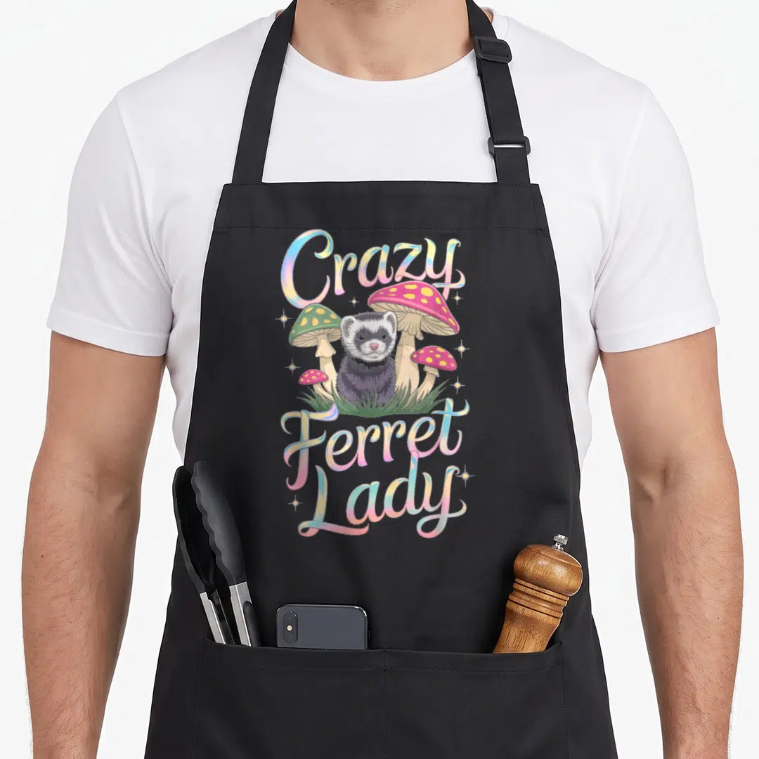 Ferret mushroom apron - Cartoon ferret in grass with pink and green mushrooms and pastel text — shown on a black cotton canvas apron against a white background
