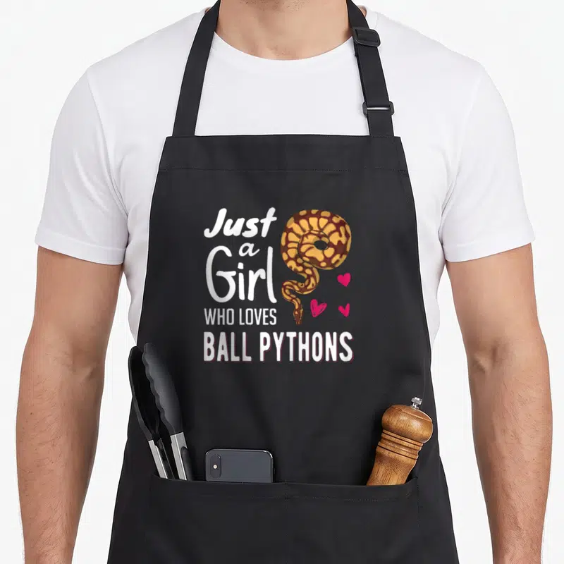 Ball snake apron - Coiled brown and yellow snake next to white text and three pink hearts — shown on a black cotton canvas apron against a white background