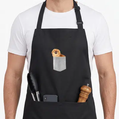 Cute pekingese dog apron - Tan Pekingese dog head peeking out of a grey printed fabric pocket design — shown on a black cotton canvas apron against a white background