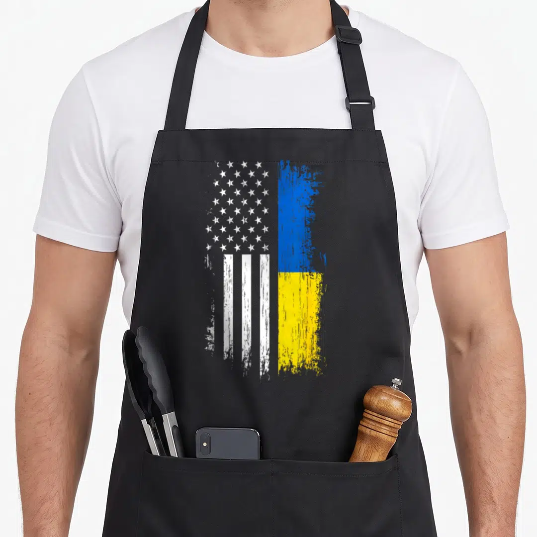 Ukraine american flag apron - Merged US and Ukraine flags in white blue yellow distressed paint style — shown on a black cotton canvas apron against a white background