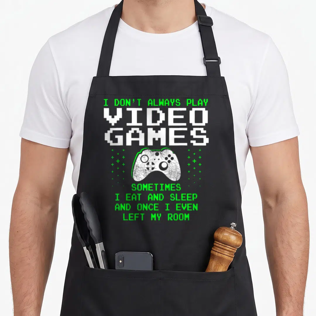 Alway gaming apron - Pixelated I DON'T ALWAYS PLAY VIDEO GAMES text surrounding a cracked white controller with green — shown on a black cotton canvas apron against a white background
