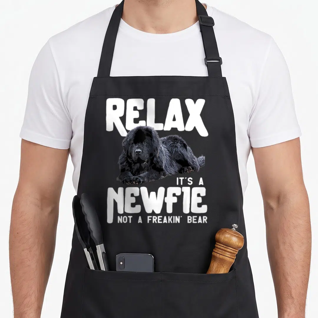 Relax dog apron - Black Newfoundland dog lying down with white text Relax Its a Newfie Not a Freakin Bear — shown on a black cotton canvas apron against a white background