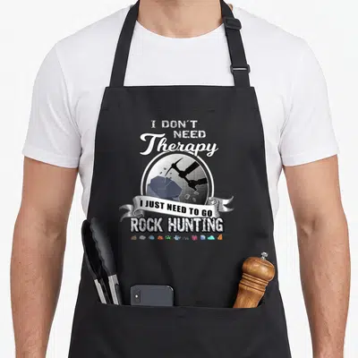 Rock my therapy apron - Distressed text I DON'T NEED Therapy I JUST NEED TO GO ROCK HUNTING with pickaxe and crystals — shown on a black cotton canvas apron against a white background