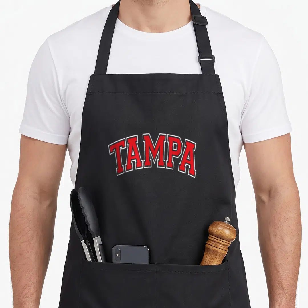 Arched tampa apron - Red arched TAMPA text with white outline on grey background — shown on a black cotton canvas apron against a white background