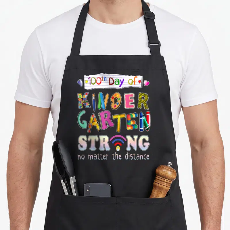 Strong kindergarten teacher apron - Multicolored 100th day of kindergarten text with school supplies and wifi symbol — shown on a black cotton canvas apron against a white background