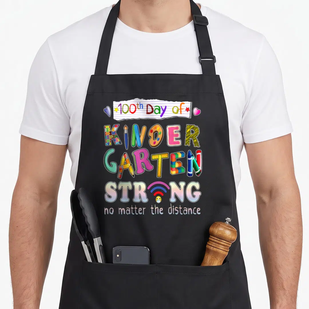 Strong kindergarten teacher apron - Multicolored 100th day of kindergarten text with school supplies and wifi symbol — shown on a black cotton canvas apron against a white background
