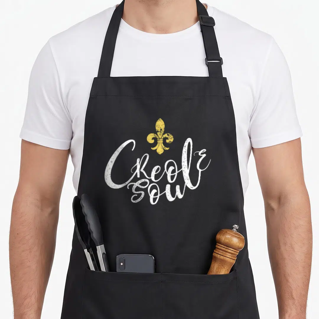 Soul cajun aprons - Yellow fleur-de-lis above white script text reading Creole Soul — shown on a black cotton canvas apron against a white background
