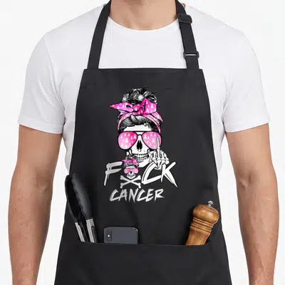 Breast messy aprons - Skeleton with messy bun and pink ribbon sunglasses flipping the bird next to text — shown on a black cotton canvas apron against a white background