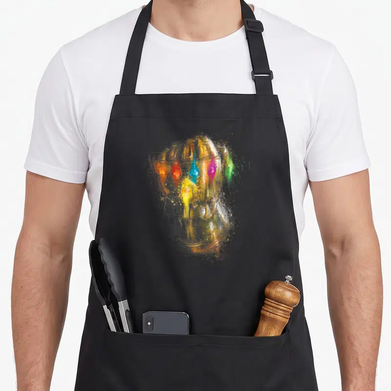 Endgame infinity apron - Watercolor golden gauntlet with colorful gems and paint splatters — shown on a black cotton canvas apron against a white background