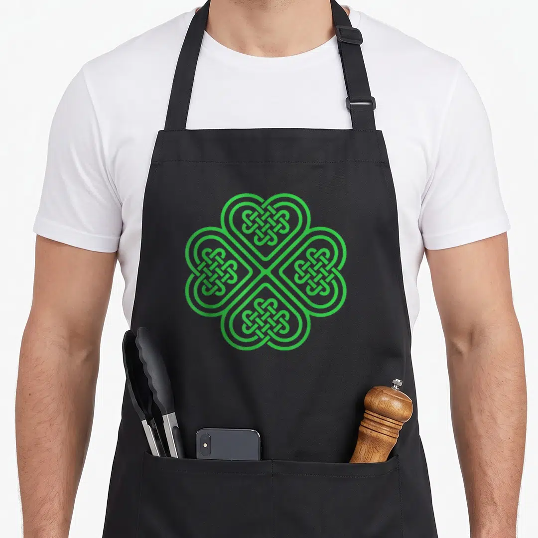 Celtic st patrick day aprons - Green Celtic knot of four interlocking hearts in a clover pattern — shown on a black cotton canvas apron against a white background
