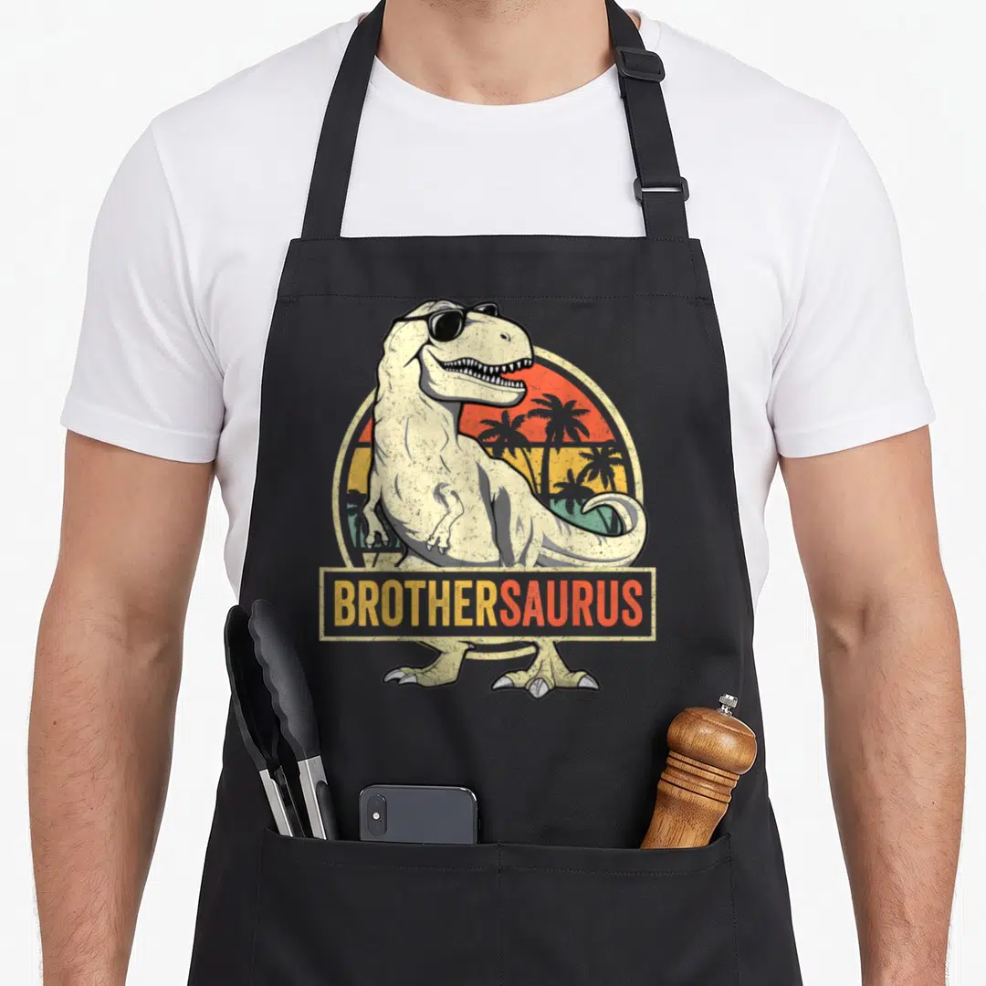 Brothersaurus t rex apron - Cartoon T-Rex sunglasses retro sunset BROTHERSAURUS text banner — shown on a black cotton canvas apron against a white background