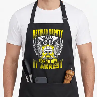 Sheriff retired police apron - Distressed yellow badge with handcuffs and text RETIRED DEPUTY SHERIFF TIME TO GIVE IT — shown on a black cotton canvas apron against a white background