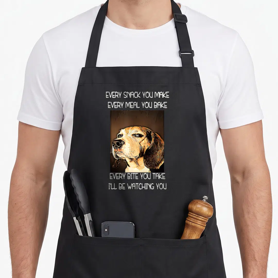 Watching beagle apron - Cartoon dog head with text about watching every snack and meal taken — shown on a black cotton canvas apron against a white background