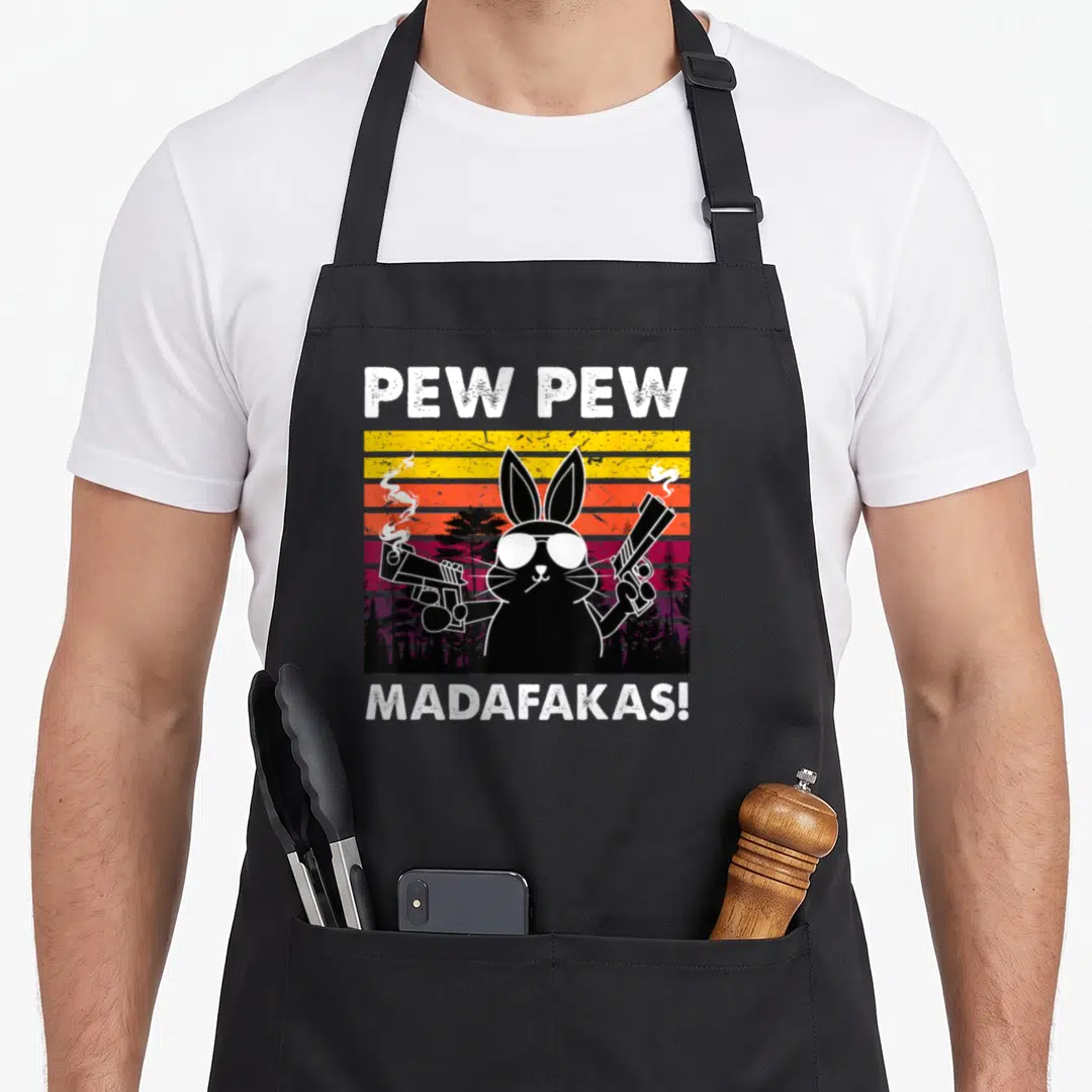 Pew bunny apron - Black rabbit with sunglasses and guns on a striped yellow orange purple sunset background — shown on a black cotton canvas apron against a white background
