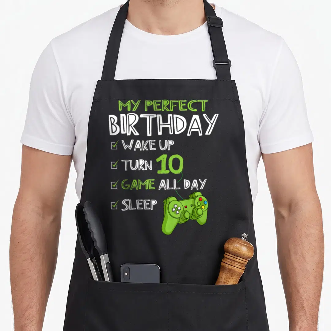 Birthday gaming aprons - Lime green controller connected by dotted line to birthday checklist text on black fabric — shown on a black cotton canvas apron against a white background