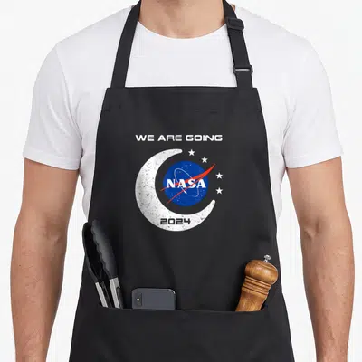 Orion nasa apron - We Are Going text above blue NASA logo inside white crescent moon with 2024 and stars — shown on a black cotton canvas apron against a white background