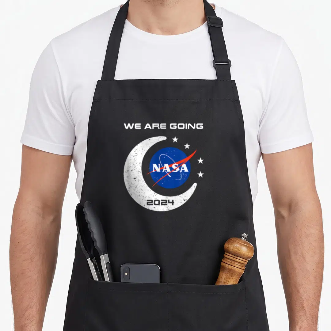 Orion nasa apron - We Are Going text above blue NASA logo inside white crescent moon with 2024 and stars — shown on a black cotton canvas apron against a white background