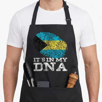 Dna bahamian apron - Fingerprint filled with Bahamian flag colors above distressed IT'S IN MY DNA text — shown on a black cotton canvas apron against a white background