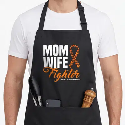 Ribbon wife apron - MOM WIFE Fighter text next to orange butterfly ribbon and MS awareness label — shown on a black cotton canvas apron against a white background