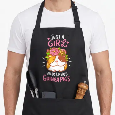 Guinea pet apron - Cartoon guinea pig with flower crown and pink text Just A Girl Who Loves Guinea Pigs — shown on a black cotton canvas apron against a white background