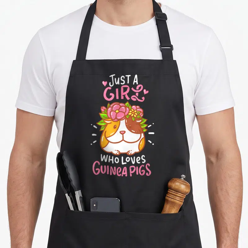 Guinea pet apron - Cartoon guinea pig with flower crown and pink text Just A Girl Who Loves Guinea Pigs — shown on a black cotton canvas apron against a white background