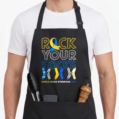 Rock chromosomes apron - Smiling yellow blue ribbon inside ROCK text above five mismatched socks in patterns — shown on a black cotton canvas apron against a white background
