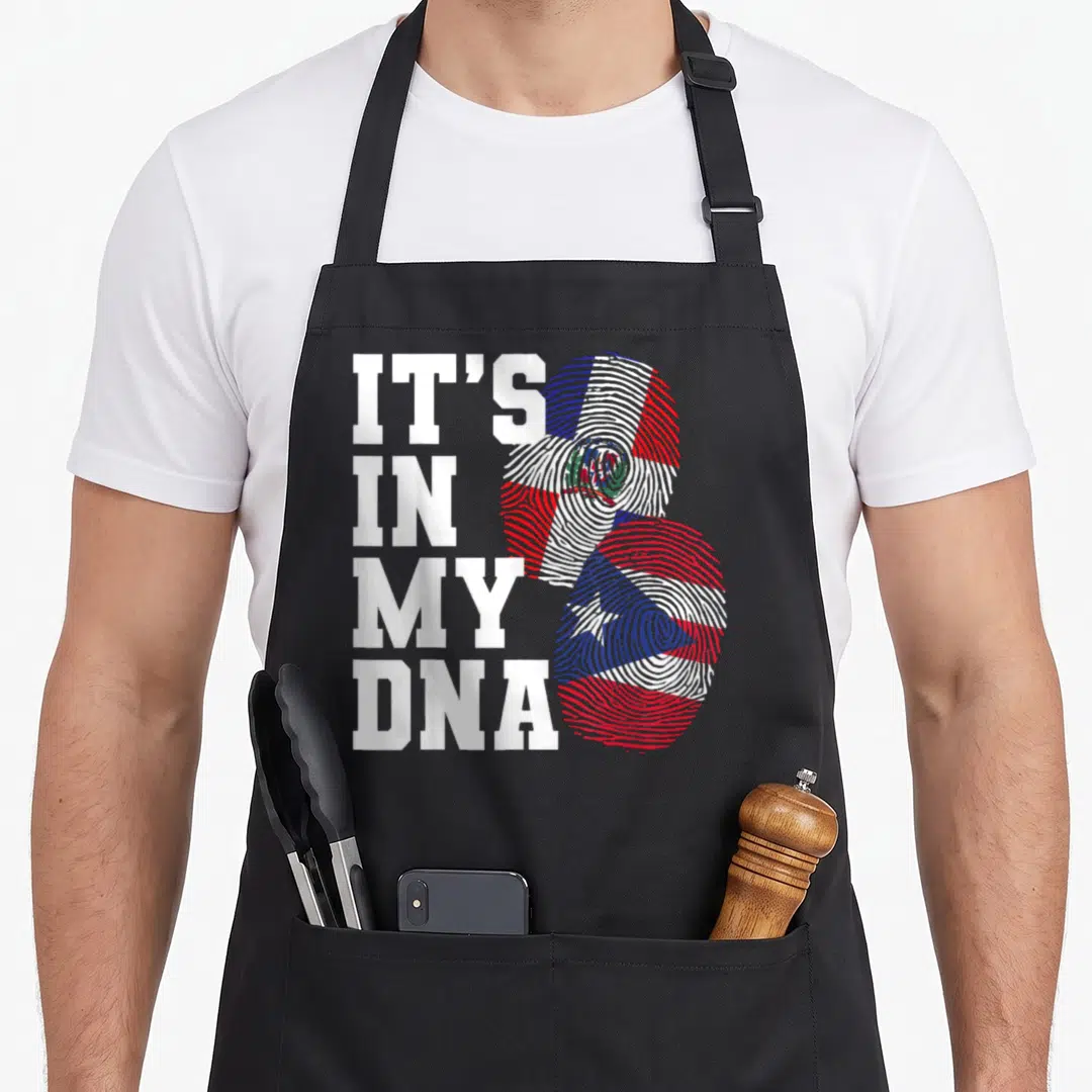 Rican heritage aprons - Stacked white text IT'S IN MY DNA next to two fingerprints filled with red white and blue flags — shown on a black cotton canvas apron against a white background