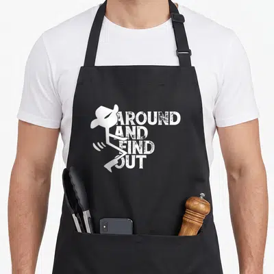 Cute around find aprons for grilling - White stick figure cowboy hat beside four stacked distressed words AROUND — shown on a black cotton canvas apron against a white background