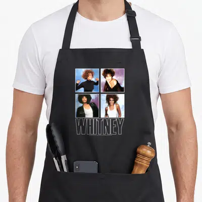 Whitney houston problem apron - Four square photos of Whitney Houston in a grid above large outlined WHITNEY text — shown on a black cotton canvas apron against a white background