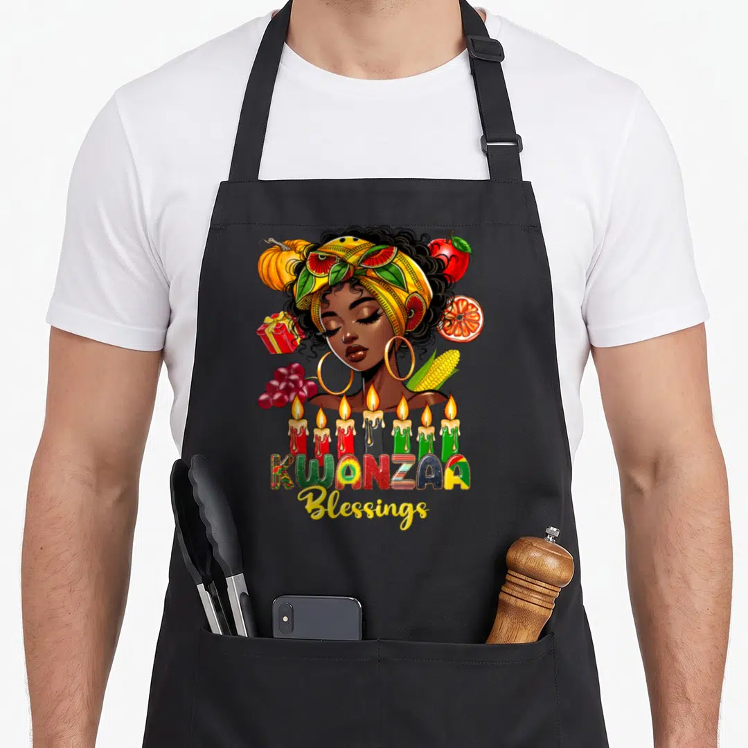 Blessing kwanzaa apron - Woman with headwrap surrounded by harvest foods and seven candles below KWANZAA Blessings text — shown on a black cotton canvas apron against a white background