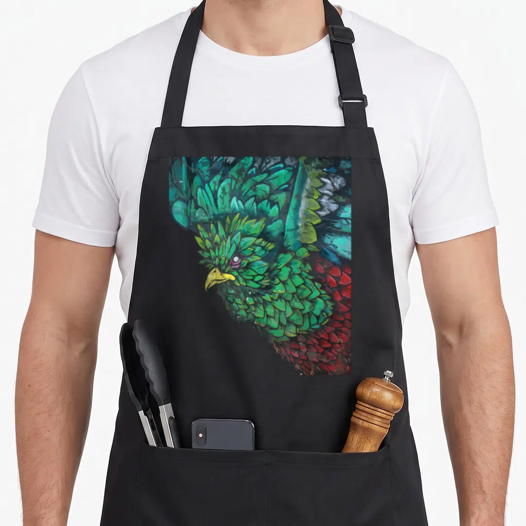 Quetzal street apron - distressed quetzal bird head art in green, red, blue, and yellow — shown on a black cotton canvas apron against a white background
