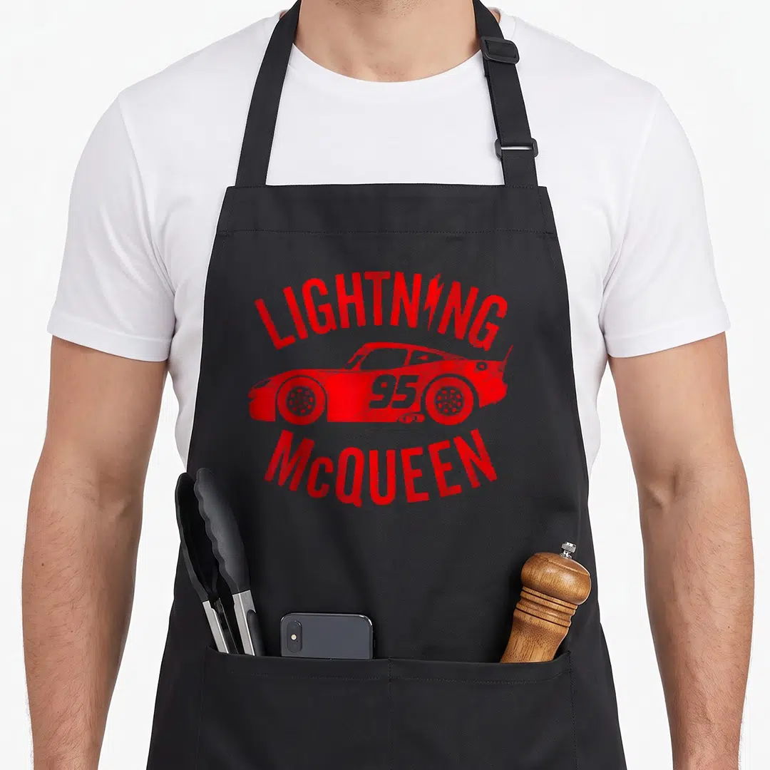 Cute race car apron - Red distressed race car with LIGHTNING 95 MCQUEEN text arching above and below — shown on a black cotton canvas apron against a white background