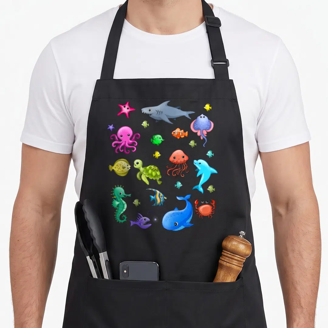 Ocean animal apron - Cartoon shark, octopus, turtle, clownfish, whale, dolphin, jellyfish, seahorse, crab, and starfish — shown on a black cotton canvas apron against a white background