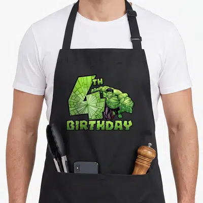 Smash birthday apron - Hulk breaking through cracked number 4 with BIRTHDAY text in green and purple — shown on a black cotton canvas apron against a white background