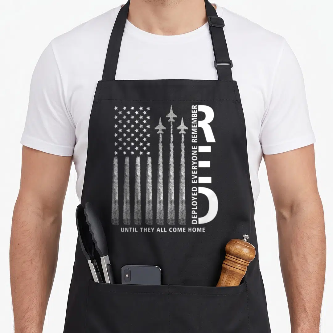 Remember american flag apron - White USA flag formed by three jet smoke trails and distressed text — shown on a black cotton canvas apron against a white background