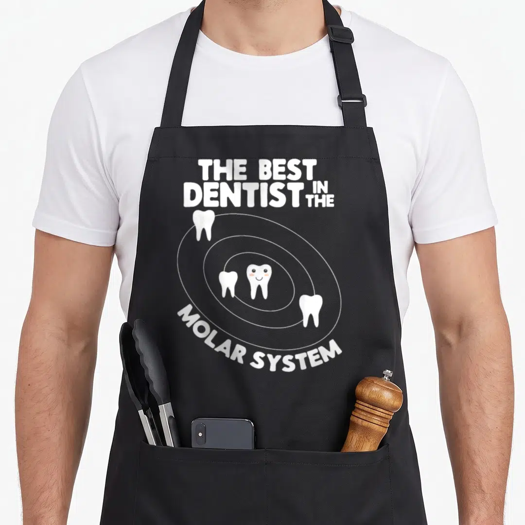 System dentist apron - White text THE BEST DENTIST IN THE MOLAR SYSTEM with four teeth orbiting a smiling center tooth — shown on a black cotton canvas apron against a white background