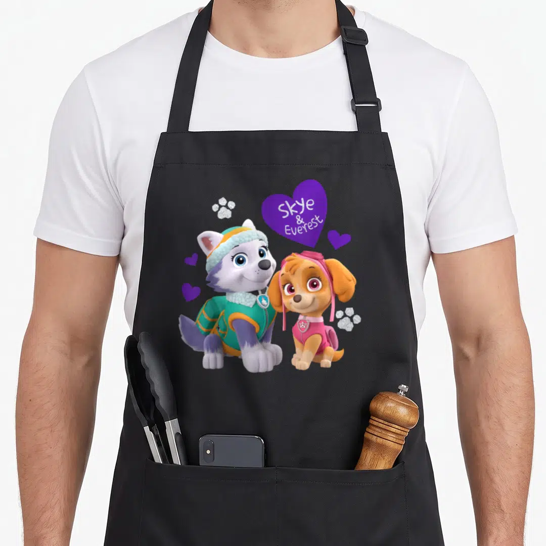 Everest isle of skye apron - Two cartoon dogs sit near a purple heart with Skye & Everest text and glittery paws — shown on a black cotton canvas apron against a white background